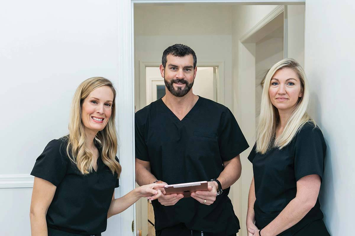 Doctor and nurses in black scrubs in front of white doorway