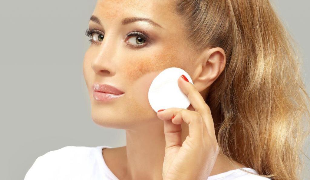 A fair skinned woman wiping a make up pad across her face