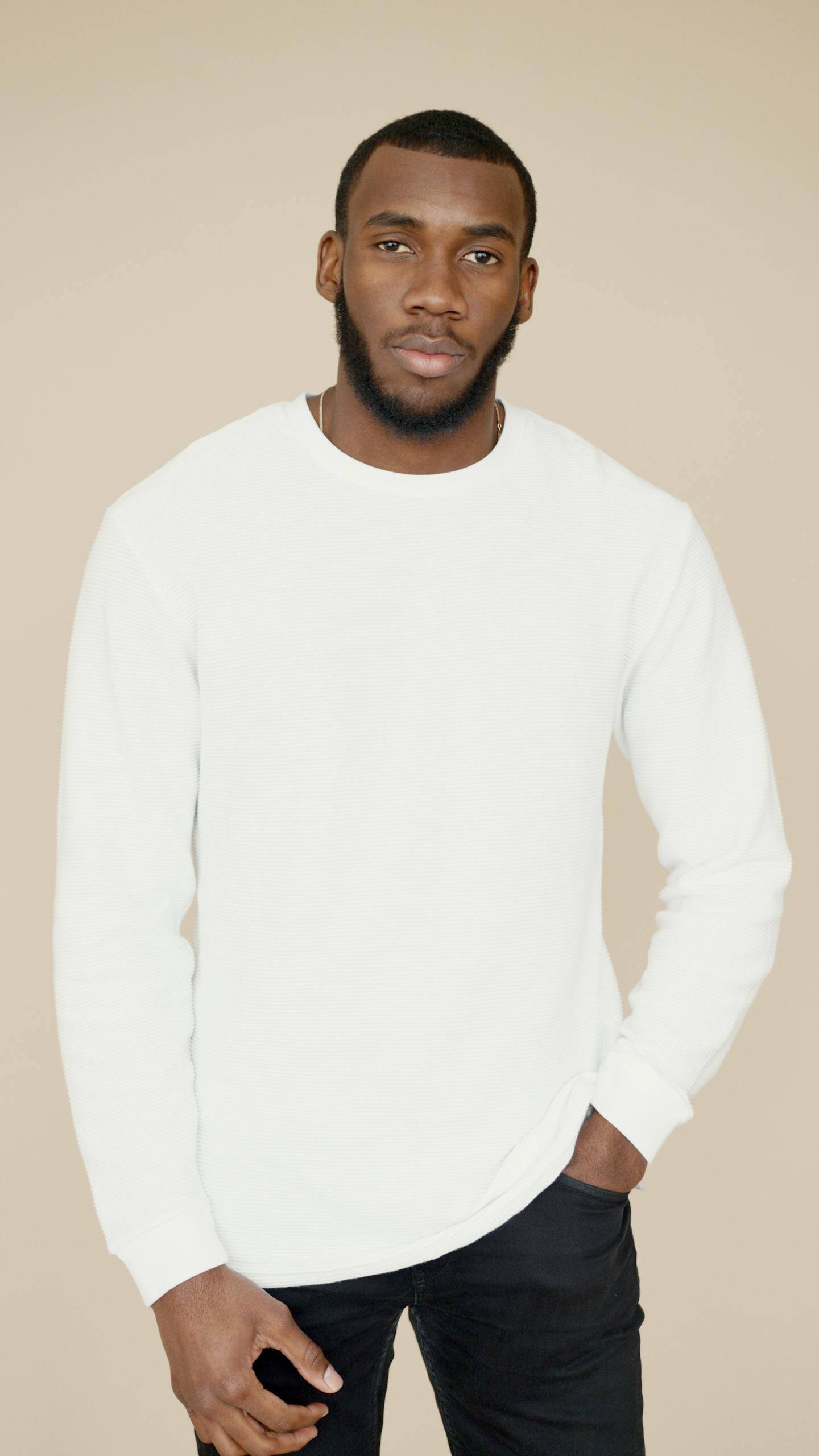 Stylish portrait of a confident man in a white sweater against a neutral background.