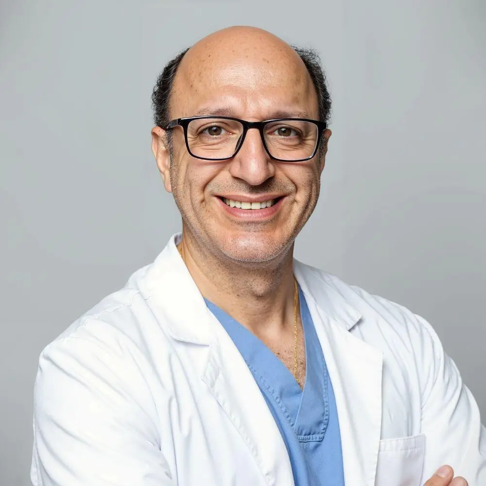Dr. Joseph Yazdi smiling wearing a white Doctors coat with blue scrubs.