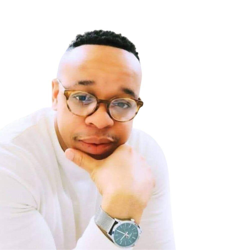 Ken posing with is hand on his face and looking on, he is wearing a white shirt and glasses.